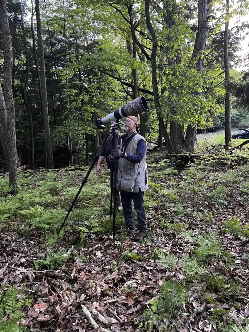 A person standing in the woods with a camera.